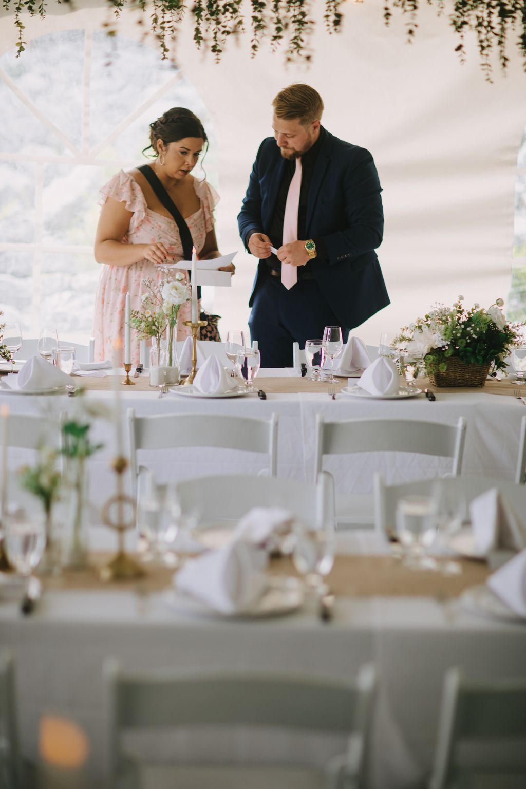 Bride in pink lace and groom in navy blazer exchange vows at elegant white tablescape with hanging greenery