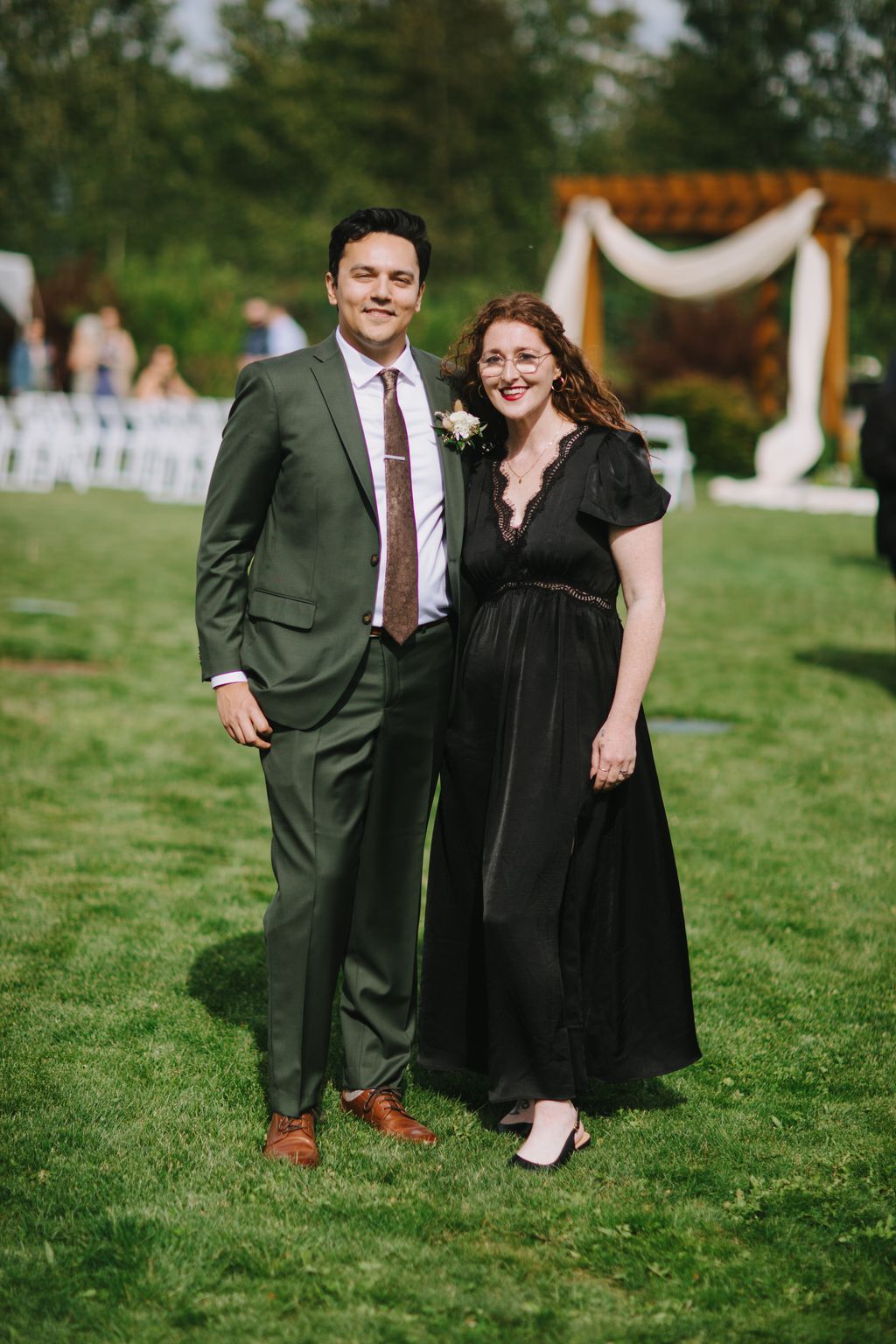 Couple in formal attire posing on grass at outdoor garden wedding venue with soft natural light