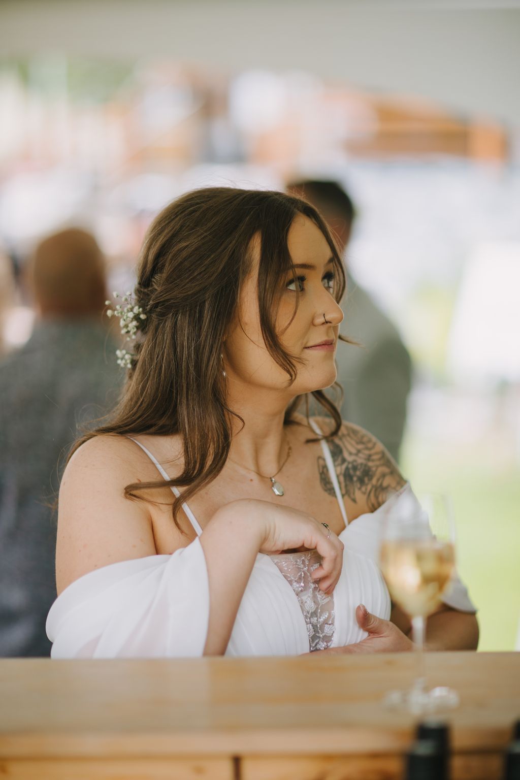 Bride in white lace dress gazes thoughtfully to the side, pearl hair accessory and nose ring visible, warm natural light