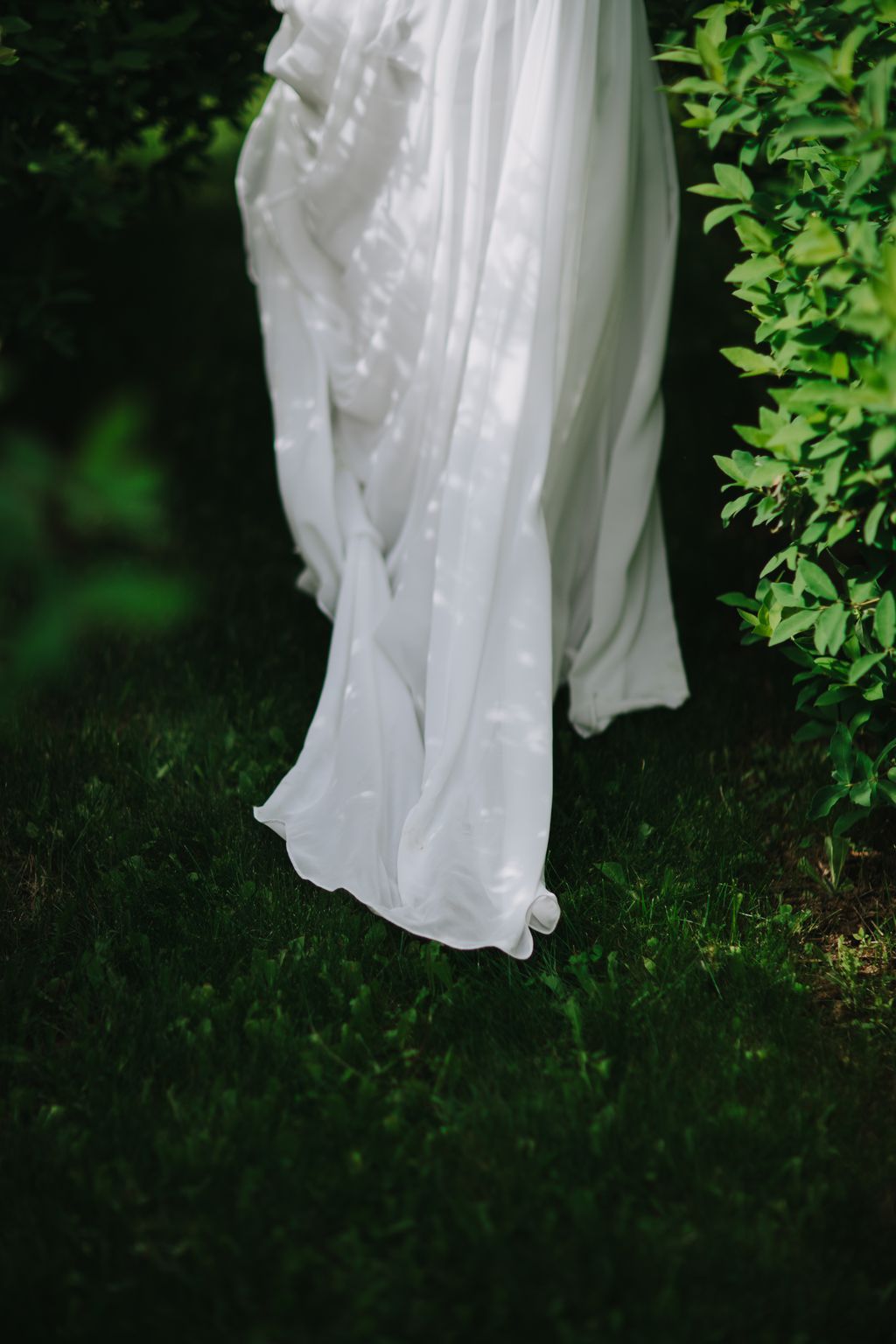 Delicate white wedding dress hem with beaded details pooling on lush green grass