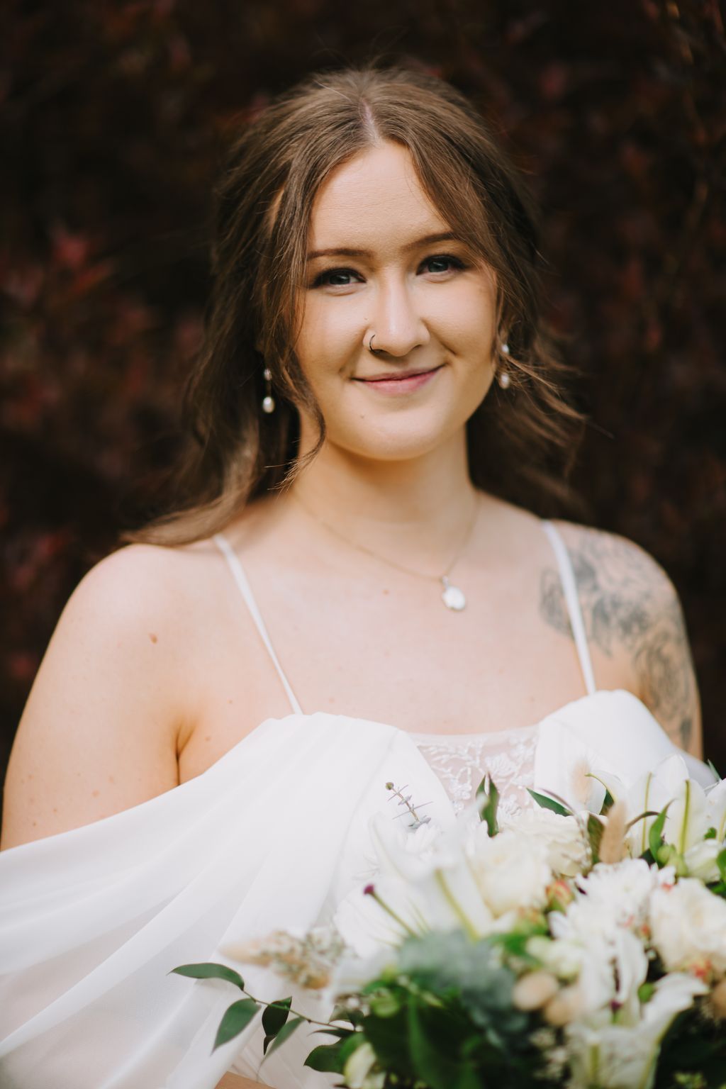 Bride in white dress holding white flowers smiles warmly at camera with soft natural light and blurred background