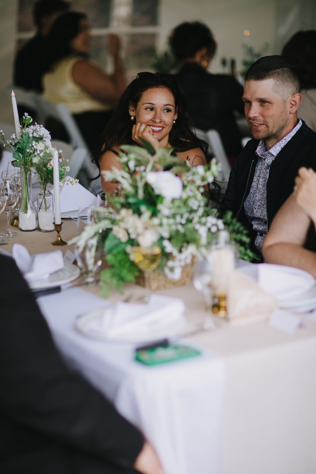 Smiling woman at elegant white table with white floral centerpiece and green napkins at wedding reception
