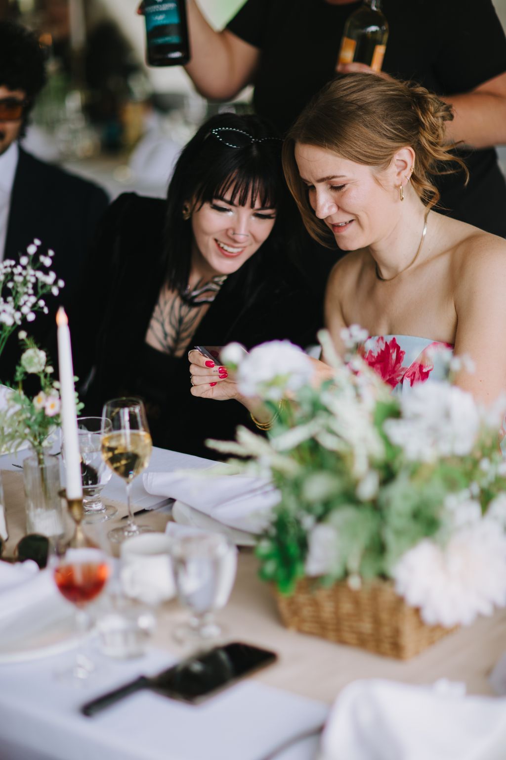 Two women smile warmly at a formal dinner table decorated with white flowers and place settings