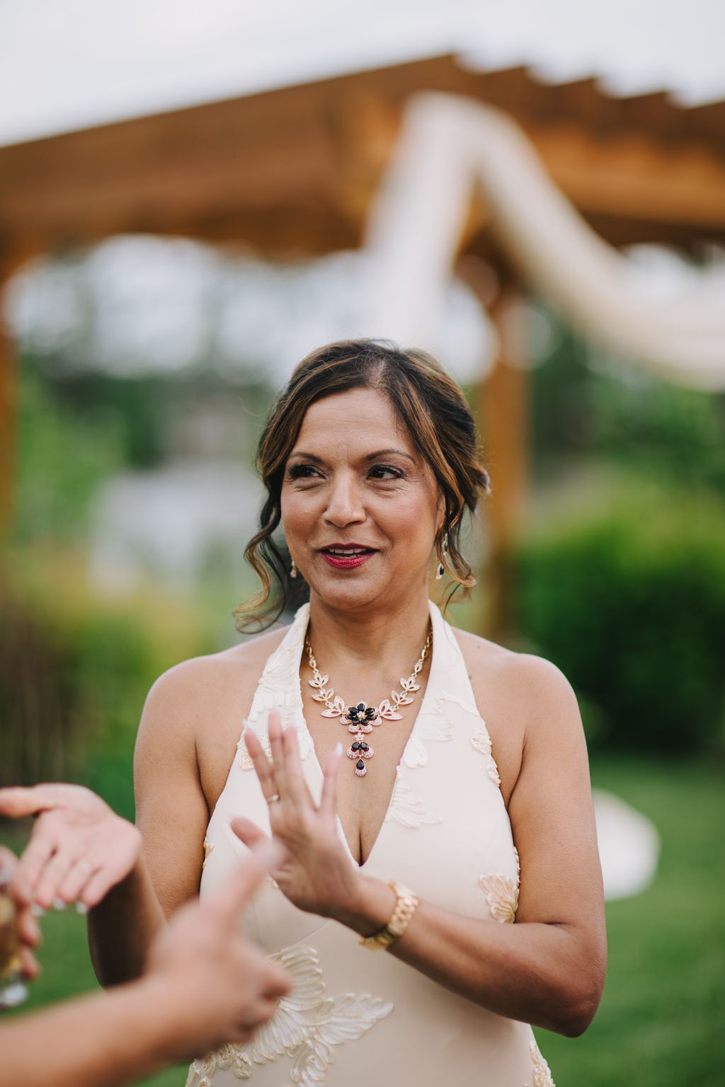 Bride in blush halter gown with ornate necklace smiles outdoors with horse and barn in soft focus background