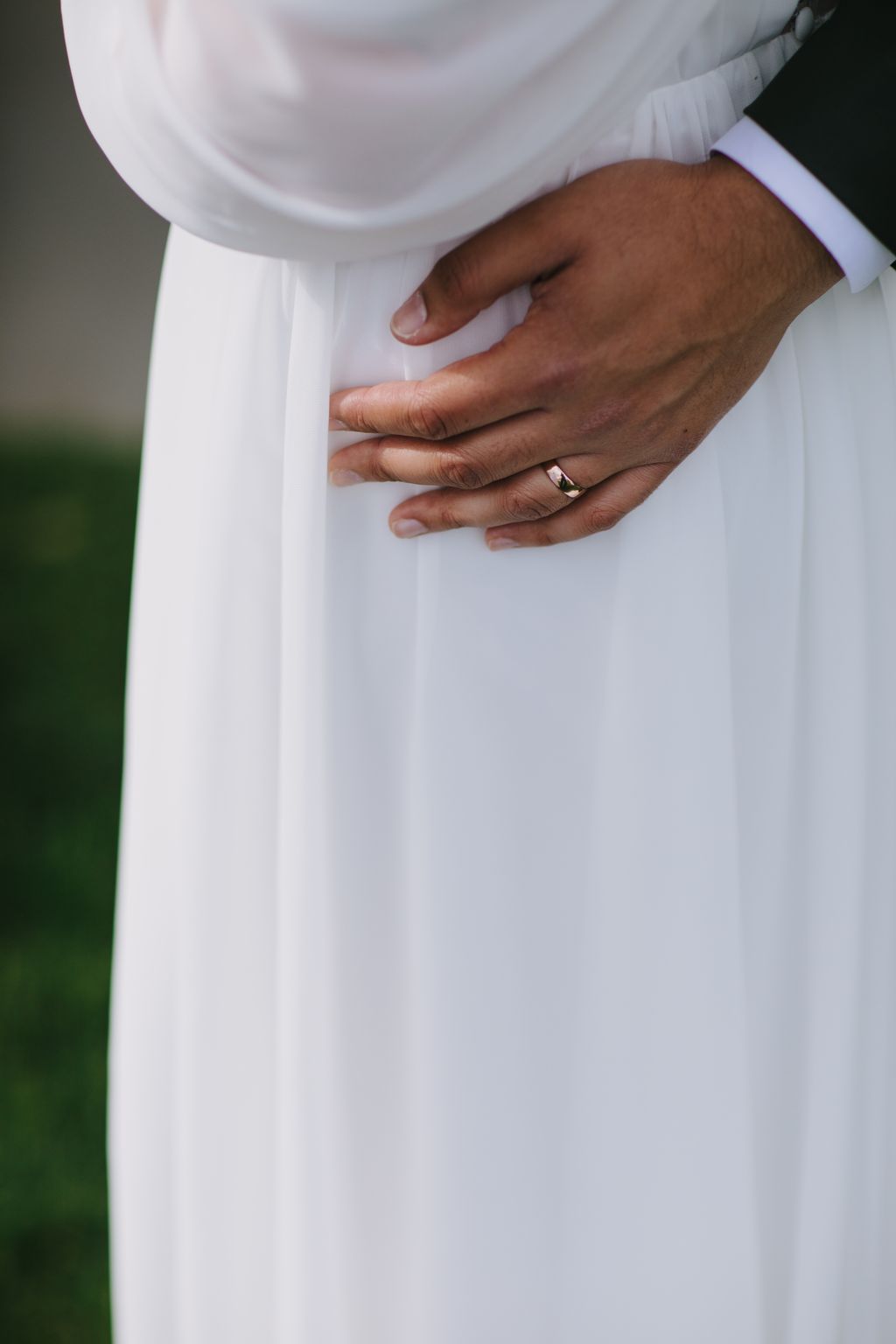 Bride and groom''s hands with wedding rings resting on white bridal gown fabric in soft, natural light