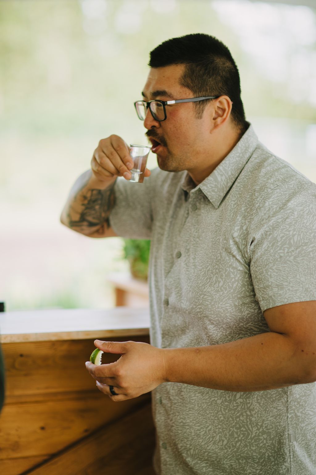 Man in glasses and light beige shirt taking a sip of water while holding a green apple, soft natural light