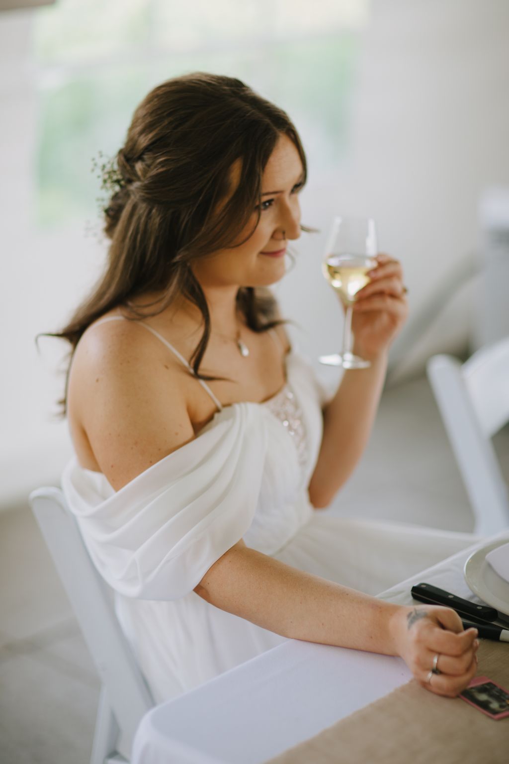 Bride in white dress holding champagne glass, gazing thoughtfully to the side in soft natural light