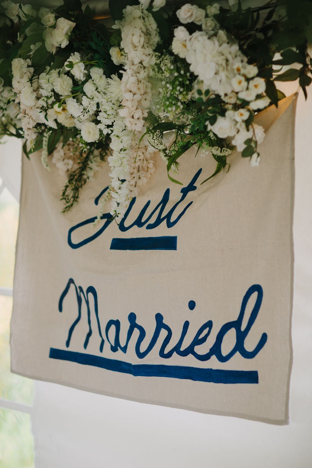 White cascading flowers with greenery arranged above navy calligraphy reading "Just Married" on cream paper