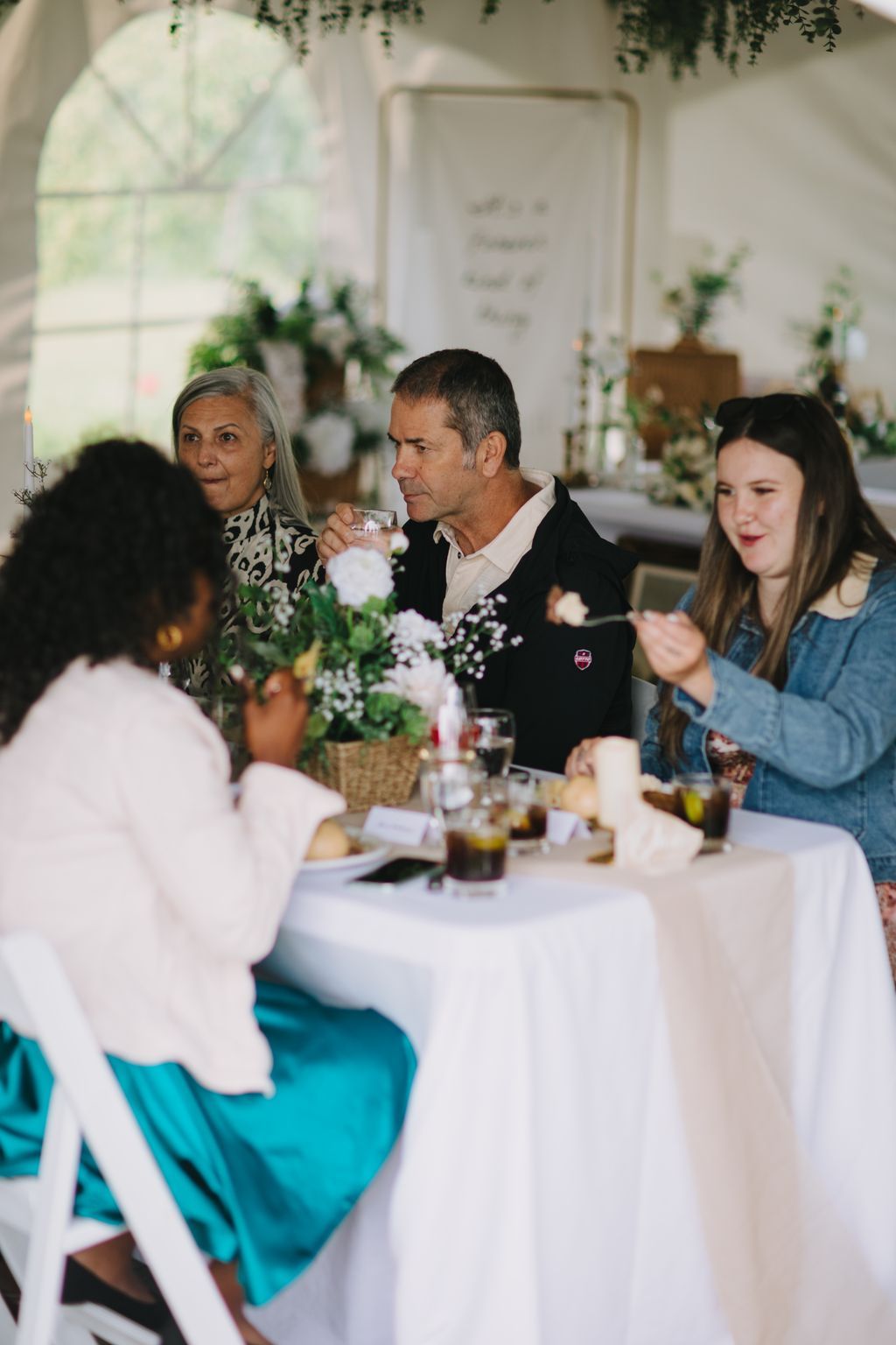 Man in black blazer holds glass during elegant reception dinner at white-draped table with floral centerpieces