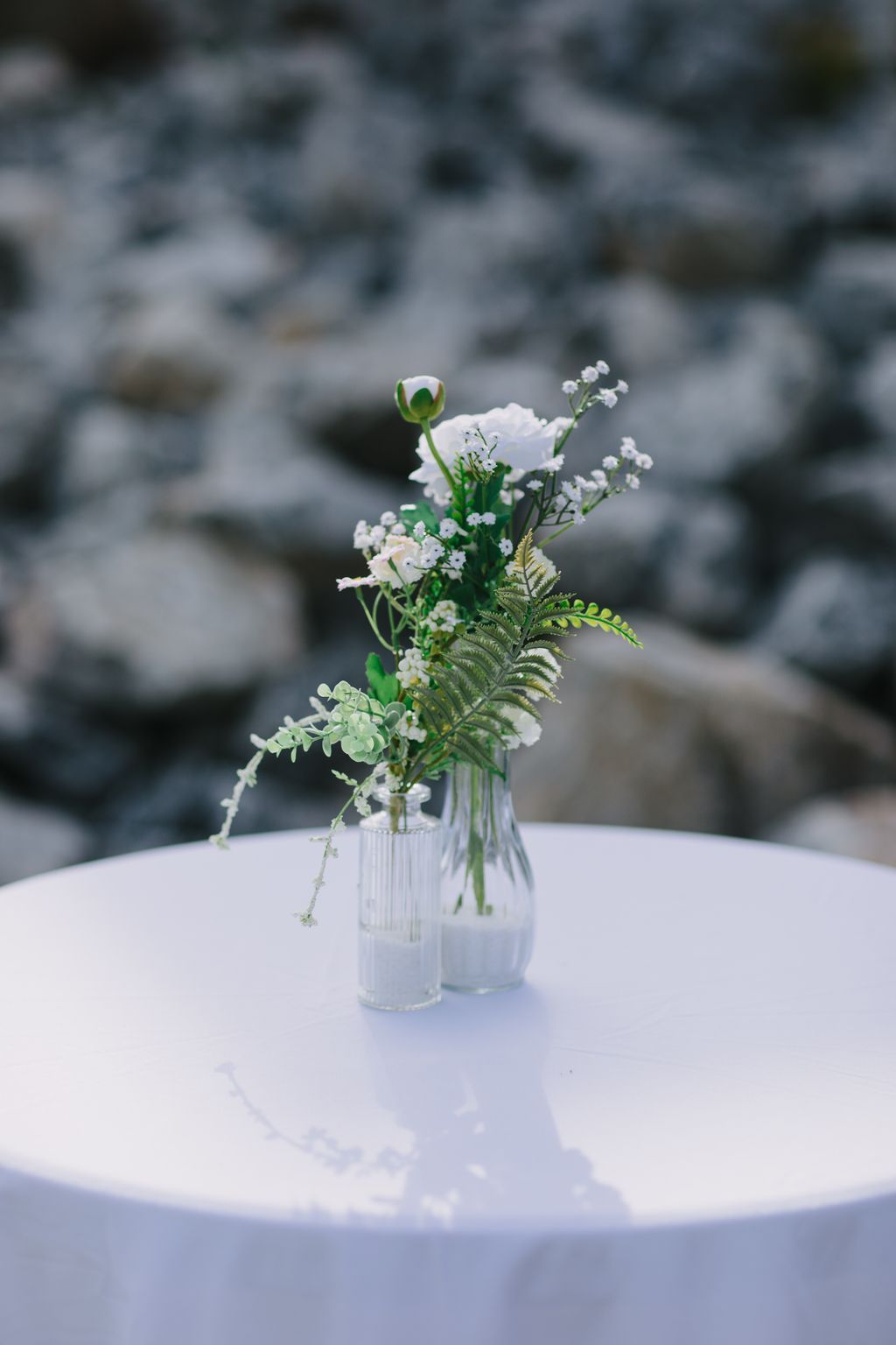 Delicate white flower arrangement with fern in a ribbed glass vase on white surface, soft blurred background
