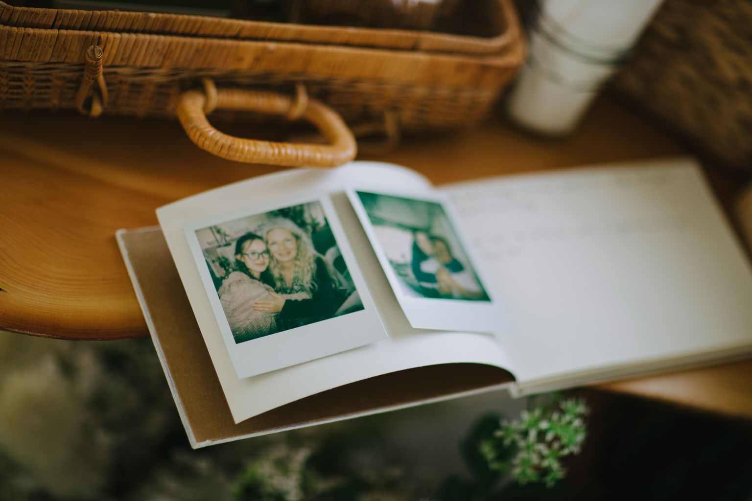 Open photo album displaying green-tinted Polaroid-style prints on white pages, with woven baskets blurred in background