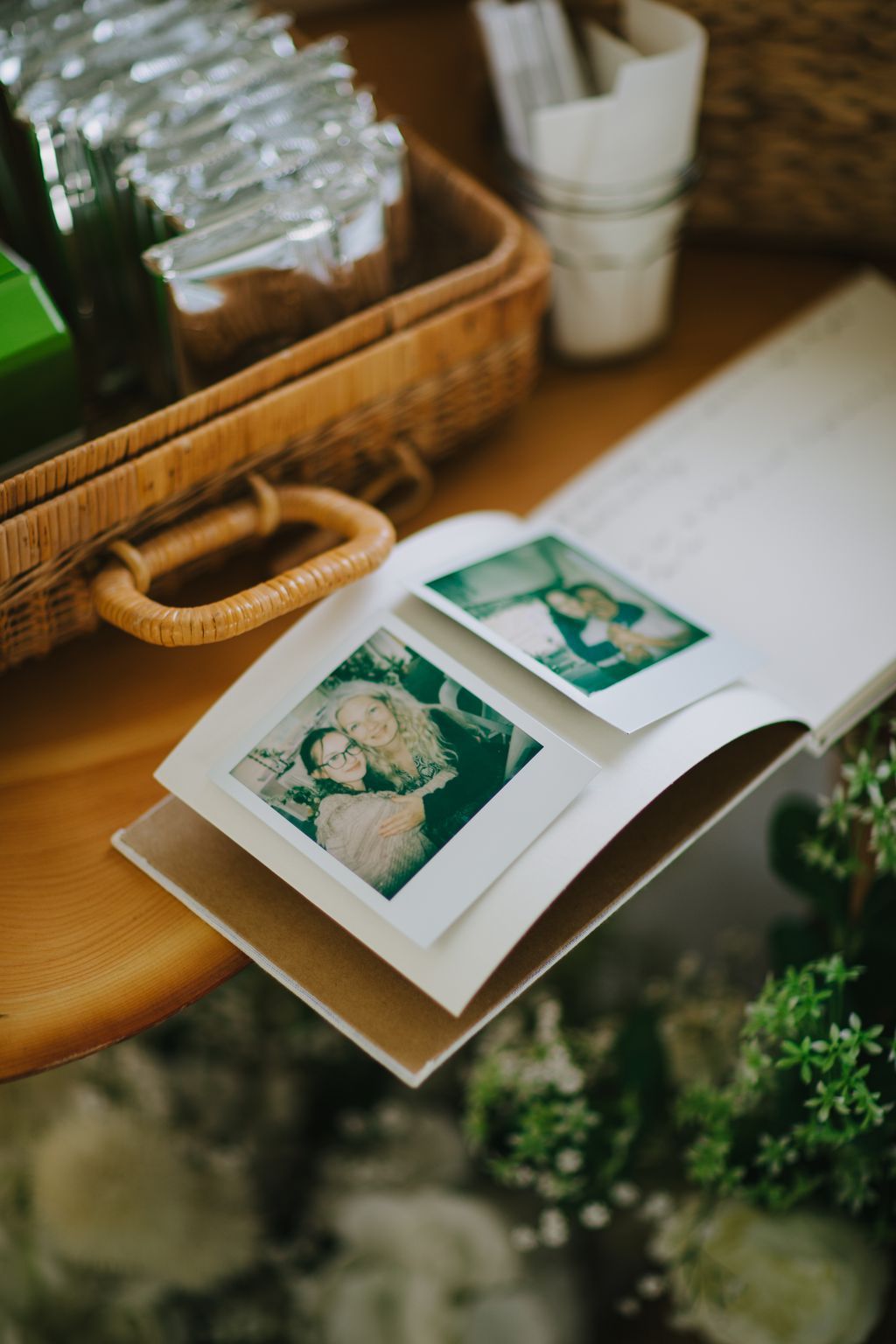 Instant film photos displayed on a wooden tray with woven basket and white flowers in soft natural light