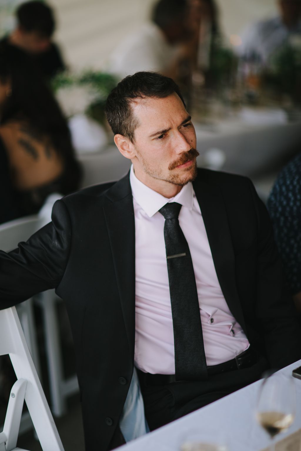 Groom in black suit and pink shirt with dark tie, looking thoughtfully to the side in soft natural light