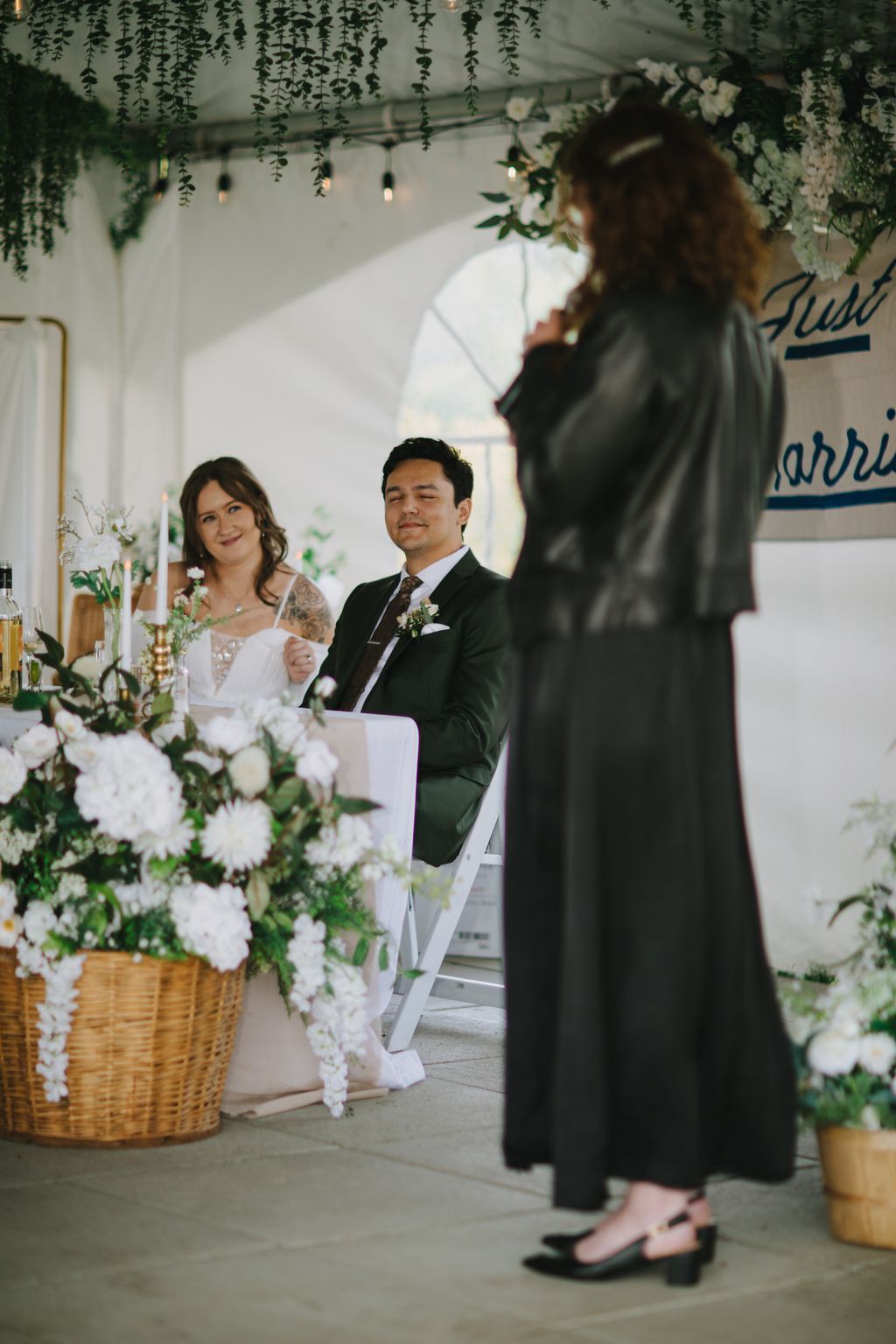 Groom gazes adoringly at bride during indoor ceremony beneath hanging greenery and pendant lights
