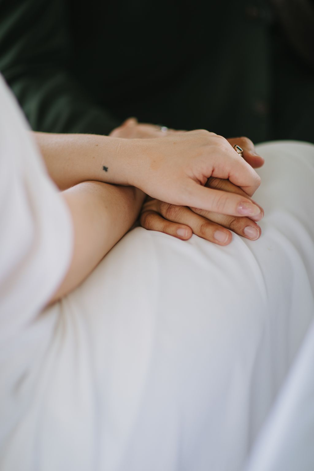 Hands stacked together showing diverse skin tones and wedding rings against white fabric, intimate moment of unity