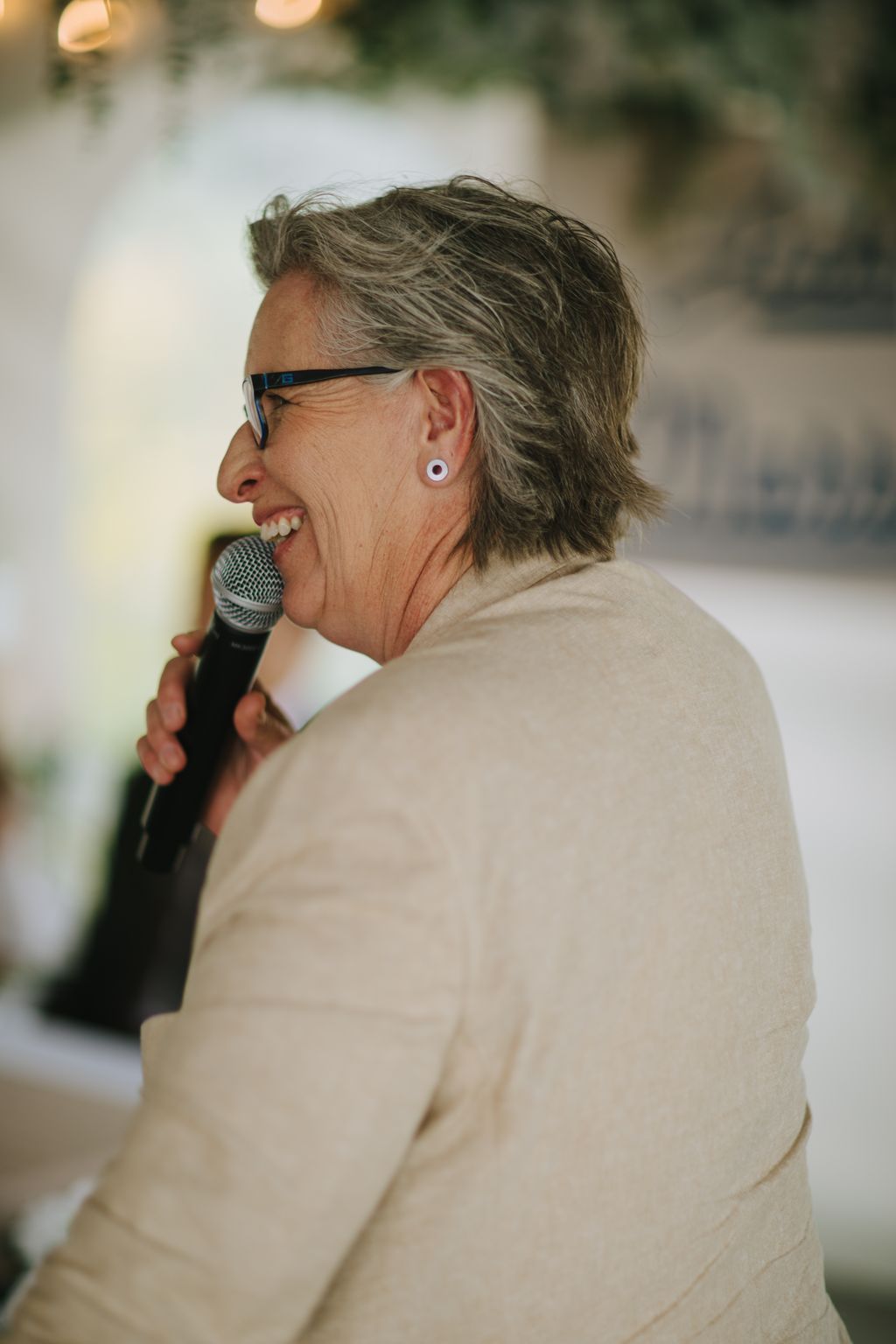 Woman speaking into microphone at wedding reception, smiling warmly in natural light