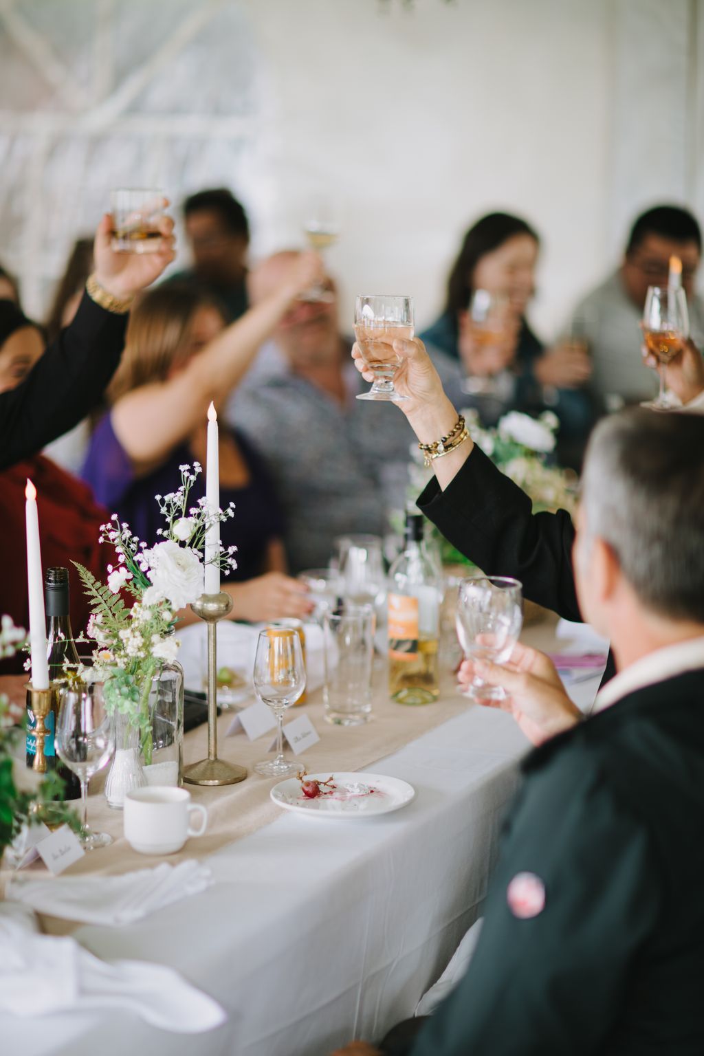 Woman raising a wine glass during a wedding reception toast, elegant table setting with white linens and floral centerpiece visible