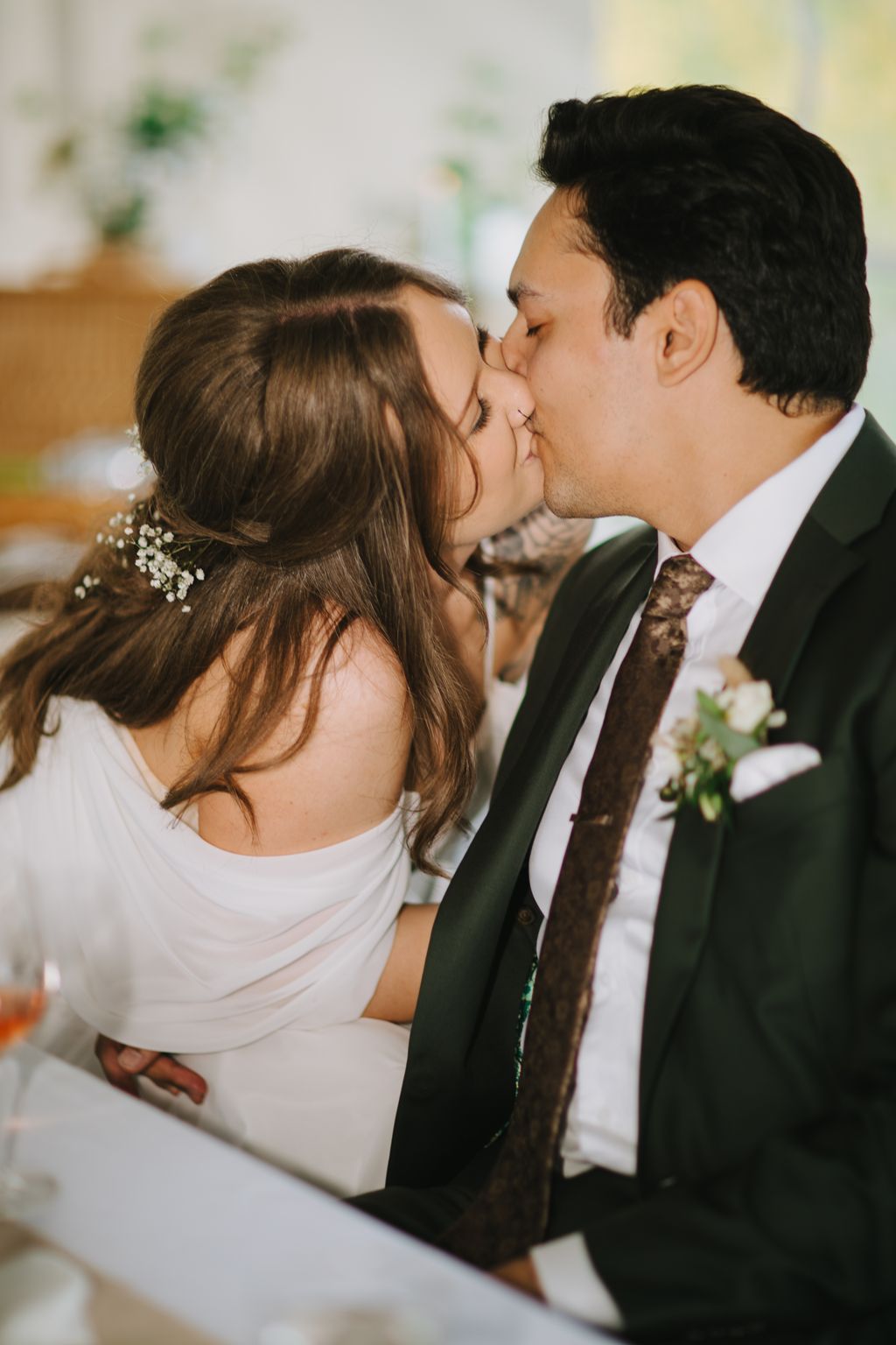 Bride and groom share a tender kiss during their wedding ceremony, soft natural light illuminating their intimate moment