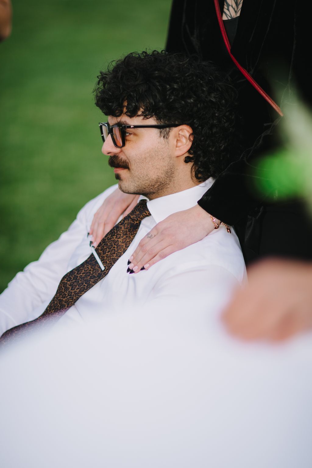 Groom in white shirt and patterned tie wearing sunglasses against bright green background, profile view