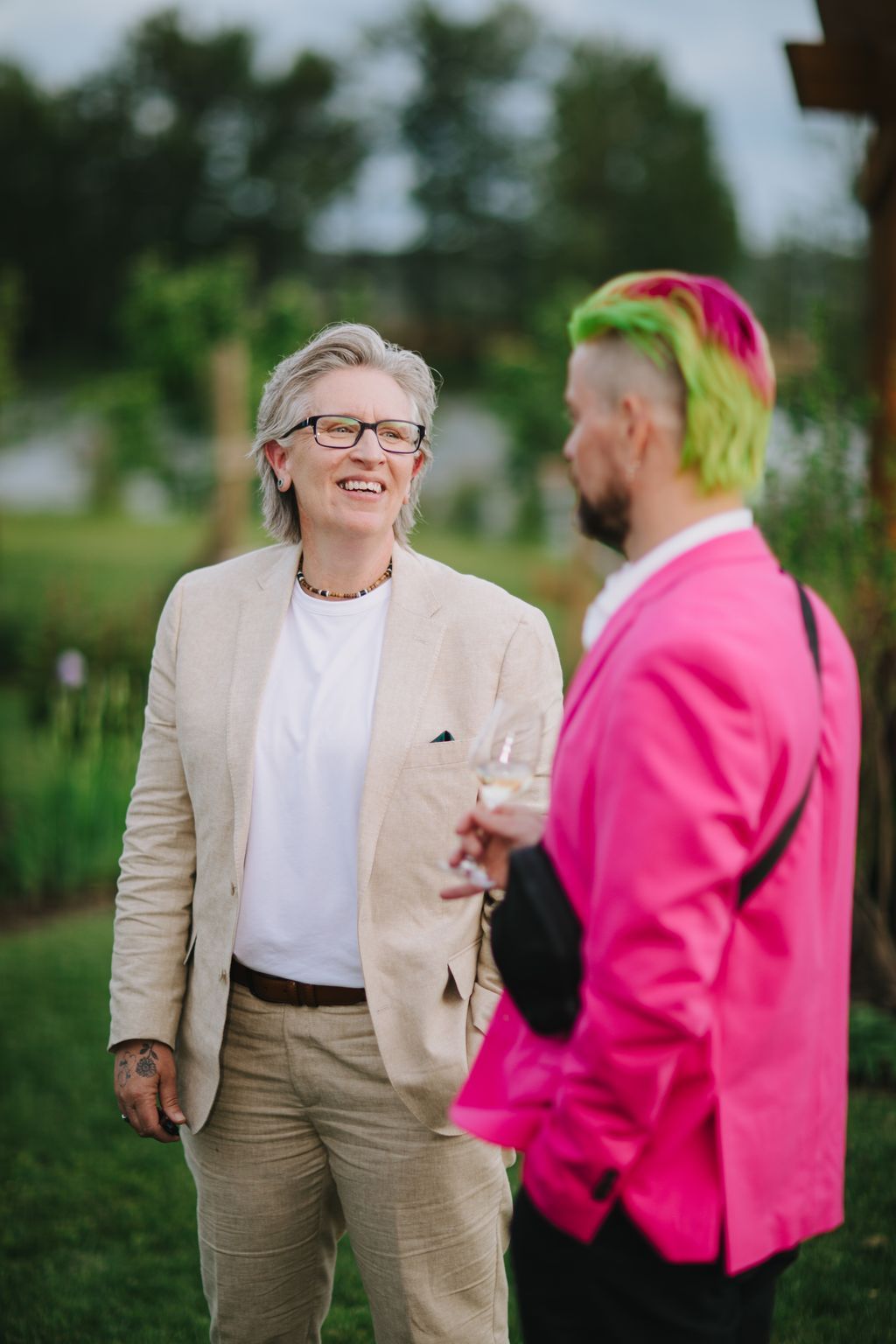 Two people smiling during an outdoor conversation, with green foliage blurred in the background