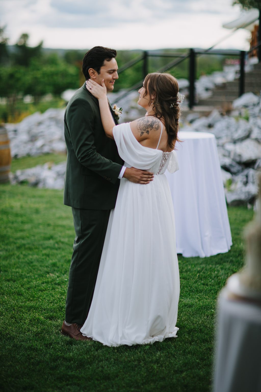 Bride and groom embracing outdoors on manicured lawn with scenic rural landscape and black fence in background