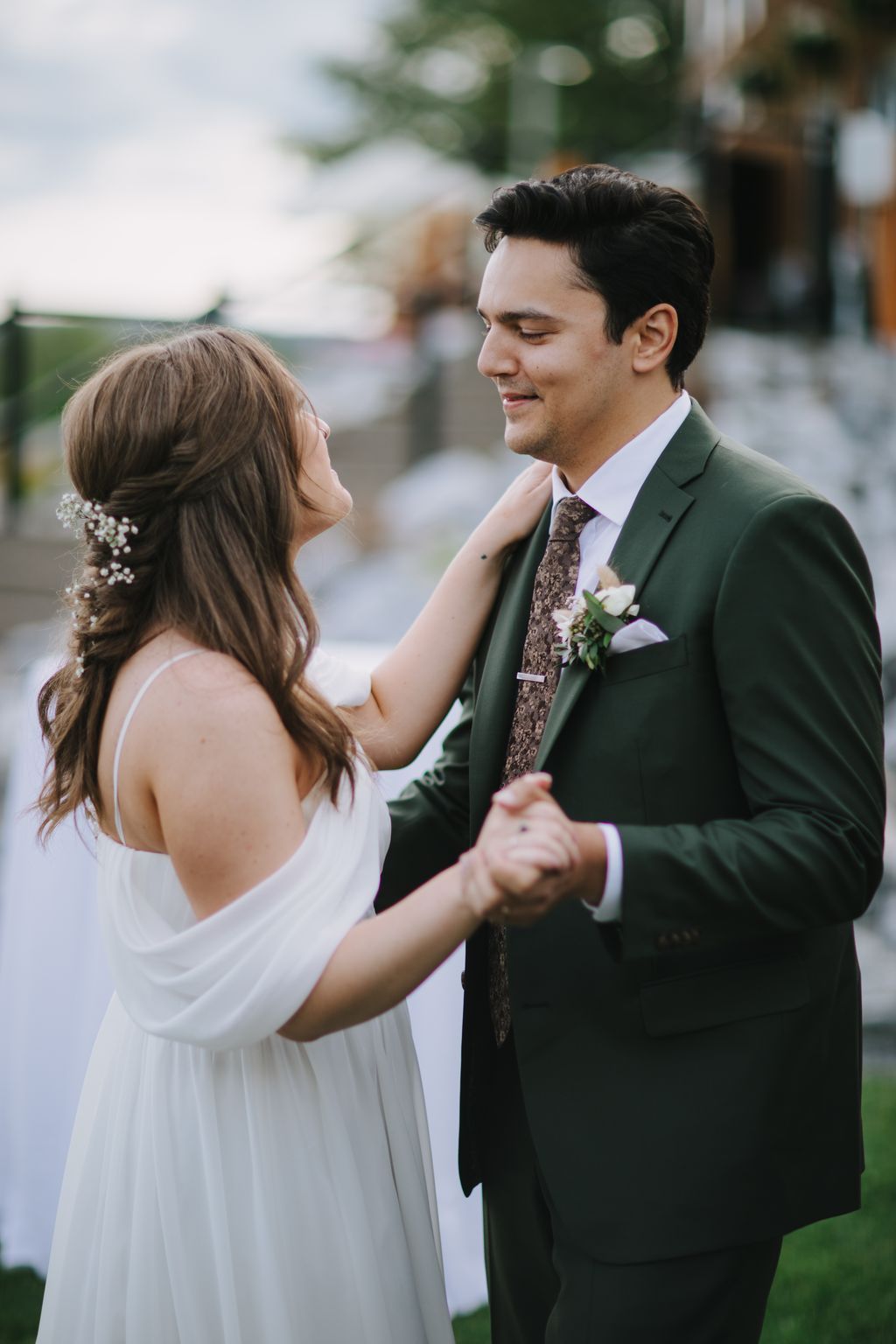 Bride in white dress touches groom''s green jacket and tie during intimate outdoor ceremony moment with soft natural light