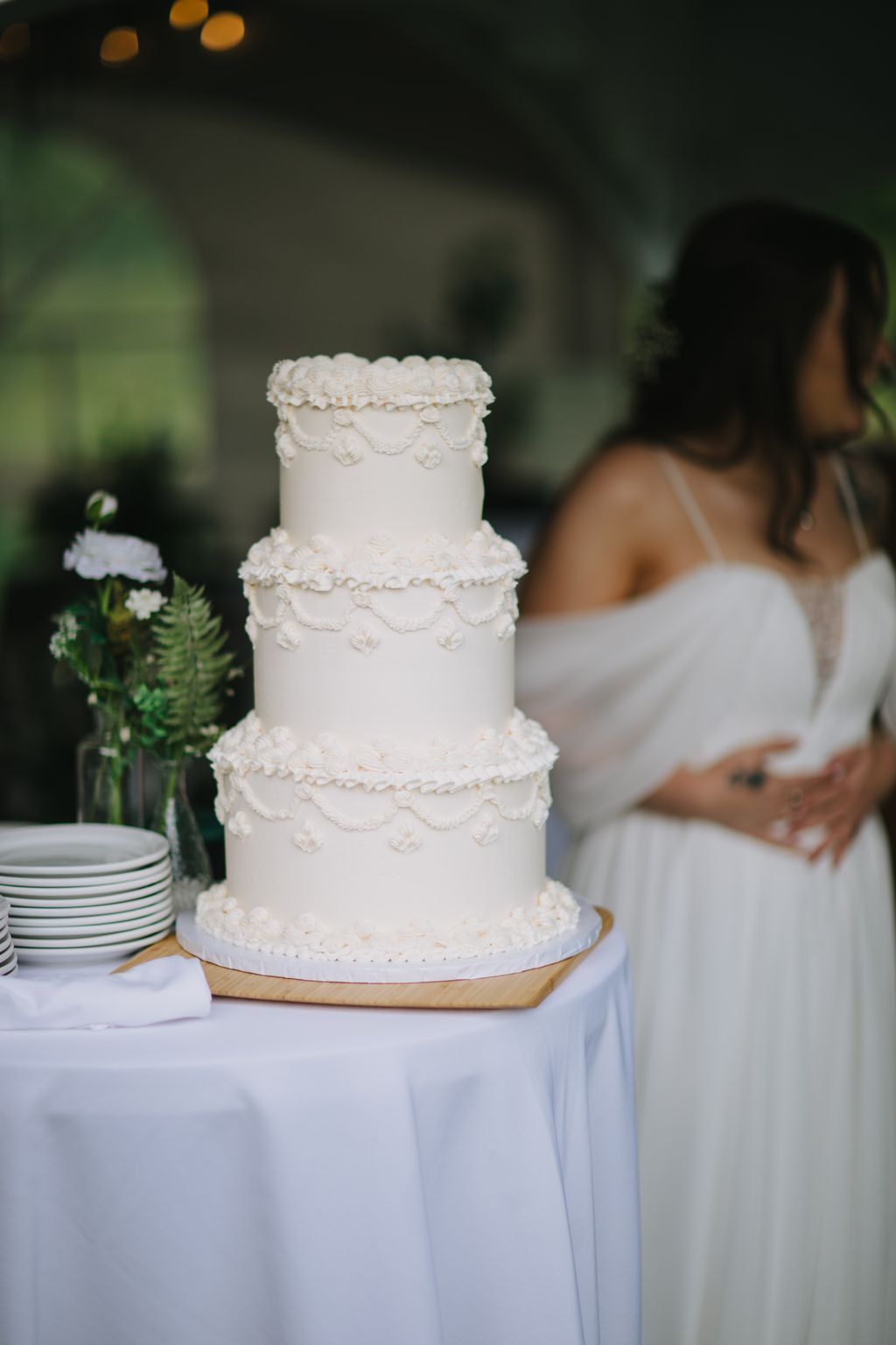 Three-tier white wedding cake with delicate piped swags and rosettes on a wooden base and draped table