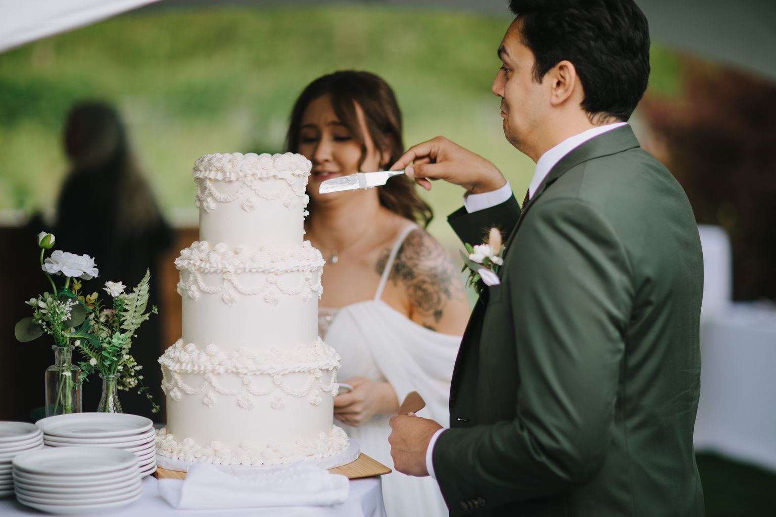 Bride and groom cut their white tiered wedding cake outdoors with a soft green background