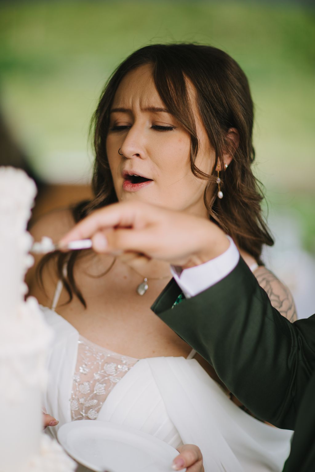 Bride in white lace dress with green cardigan smiles with eyes closed against soft green background