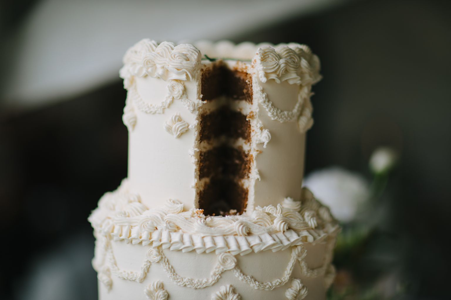 Cross-section of a multi-layered wedding cake with white frosting rosettes and decorative piping, revealing chocolate cake layers inside