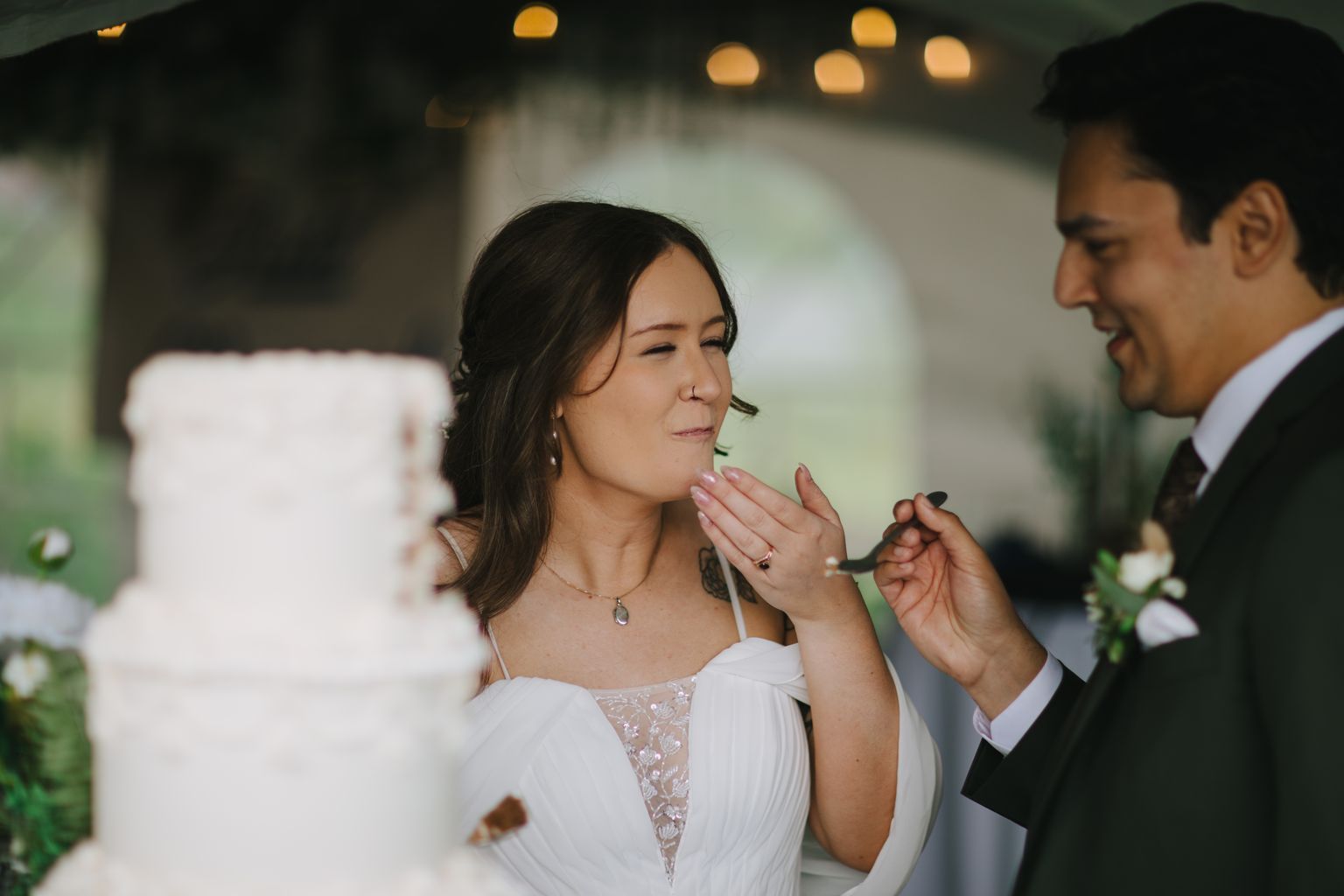 Bride in white lace dress touching her face with soft golden bokeh lights in background