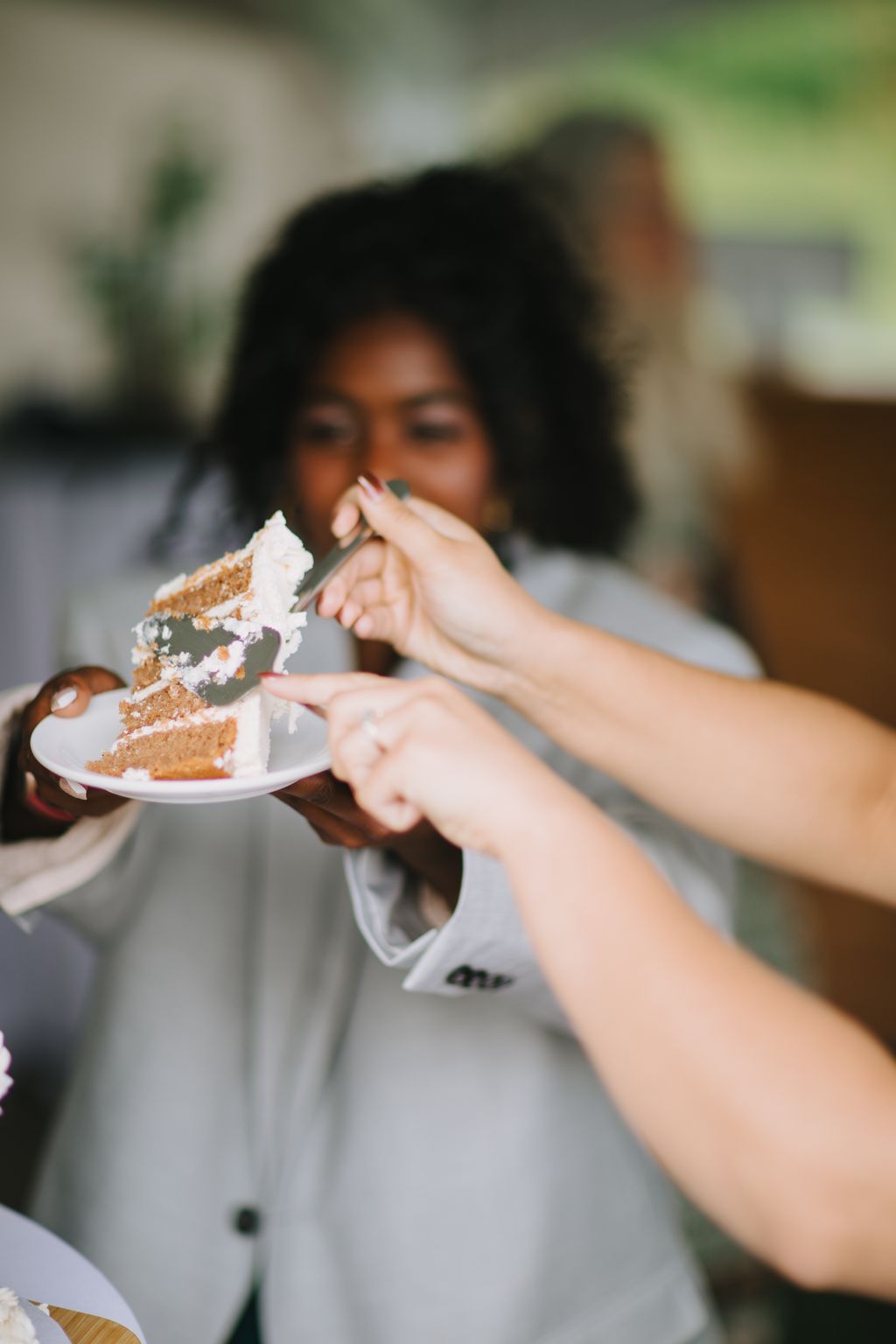 Bride and groom sharing a slice of wedding cake with soft natural light and blurred green background
