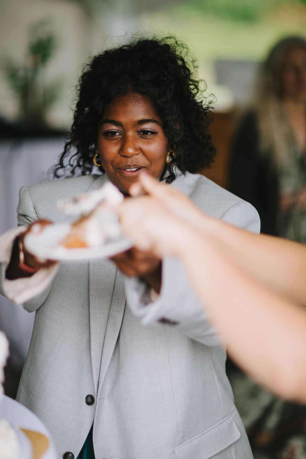 Bride in light gray blazer smiling while exchanging vows, soft natural light, intimate moment during ceremony