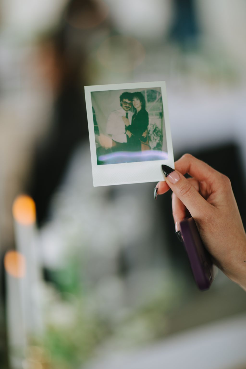 Hand holding vintage Polaroid of couple in soft-focus outdoor setting with blurred green background