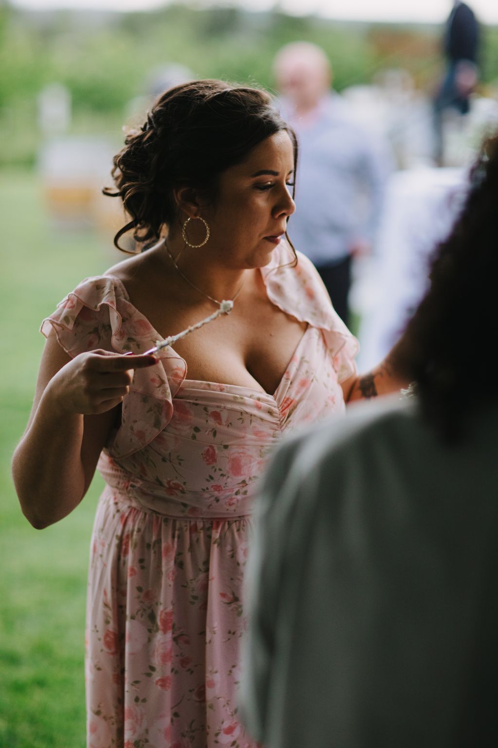 Woman in pink floral off-shoulder dress with hoop earrings gazes thoughtfully outdoors during golden hour