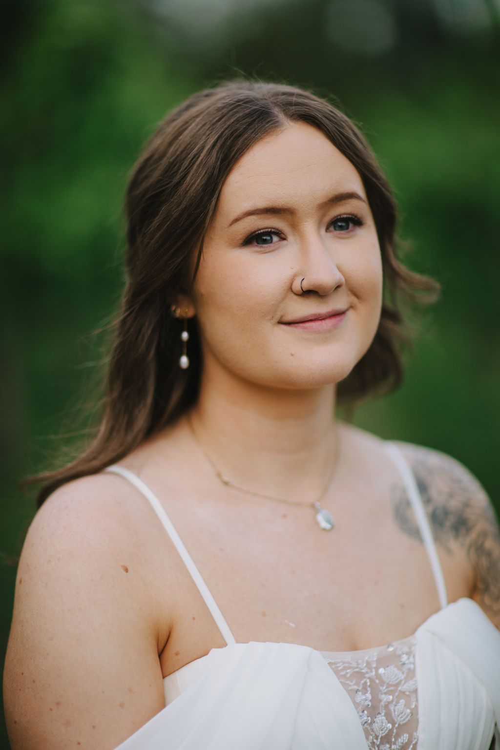 Portrait of a woman in a white bridal gown with pearl earrings against a soft green blurred background