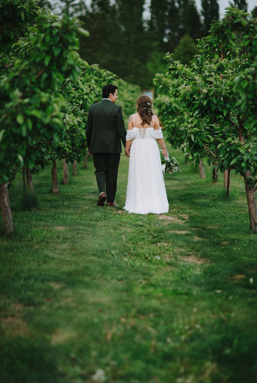 Bride and groom walking hand in hand through a lush green vineyard corridor, natural outdoor wedding portrait