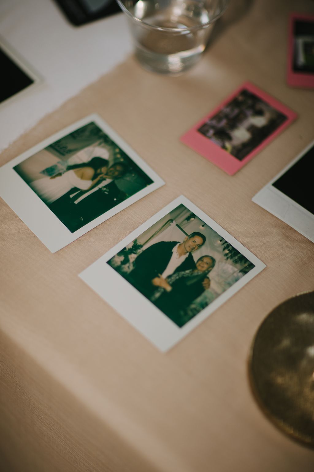 Instant film photographs scattered on a beige surface with a glass of water, capturing candid moments in warm, nostalgic tones