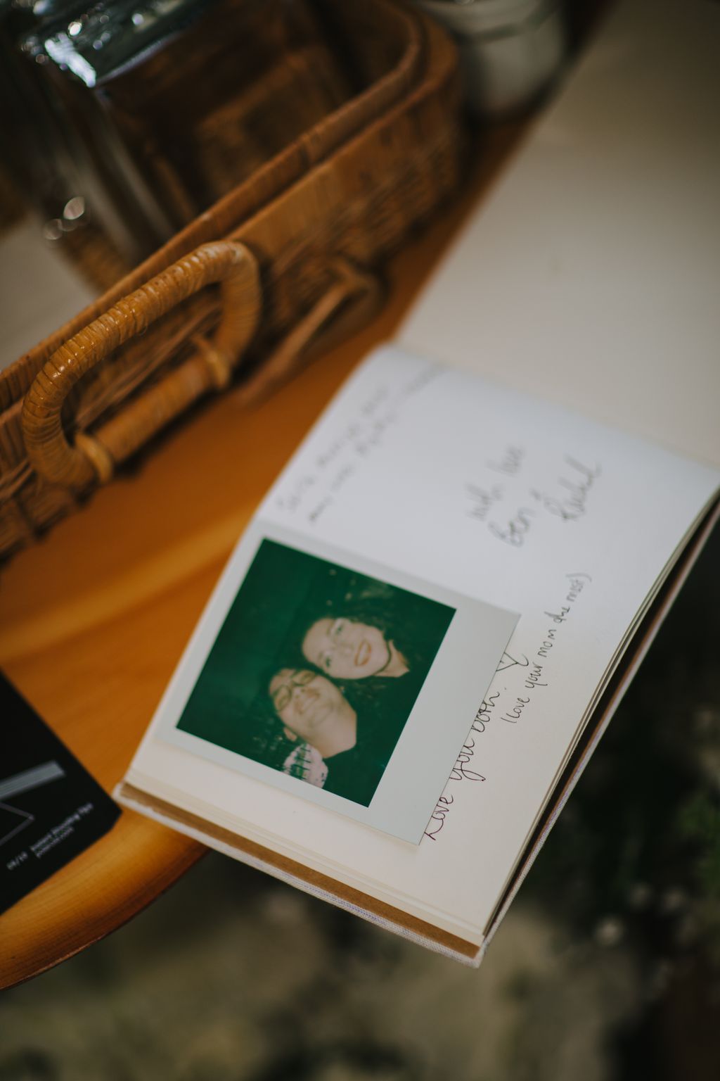 Vintage Polaroid photo of two people on an open page with handwritten text, resting on a wooden surface with carved details