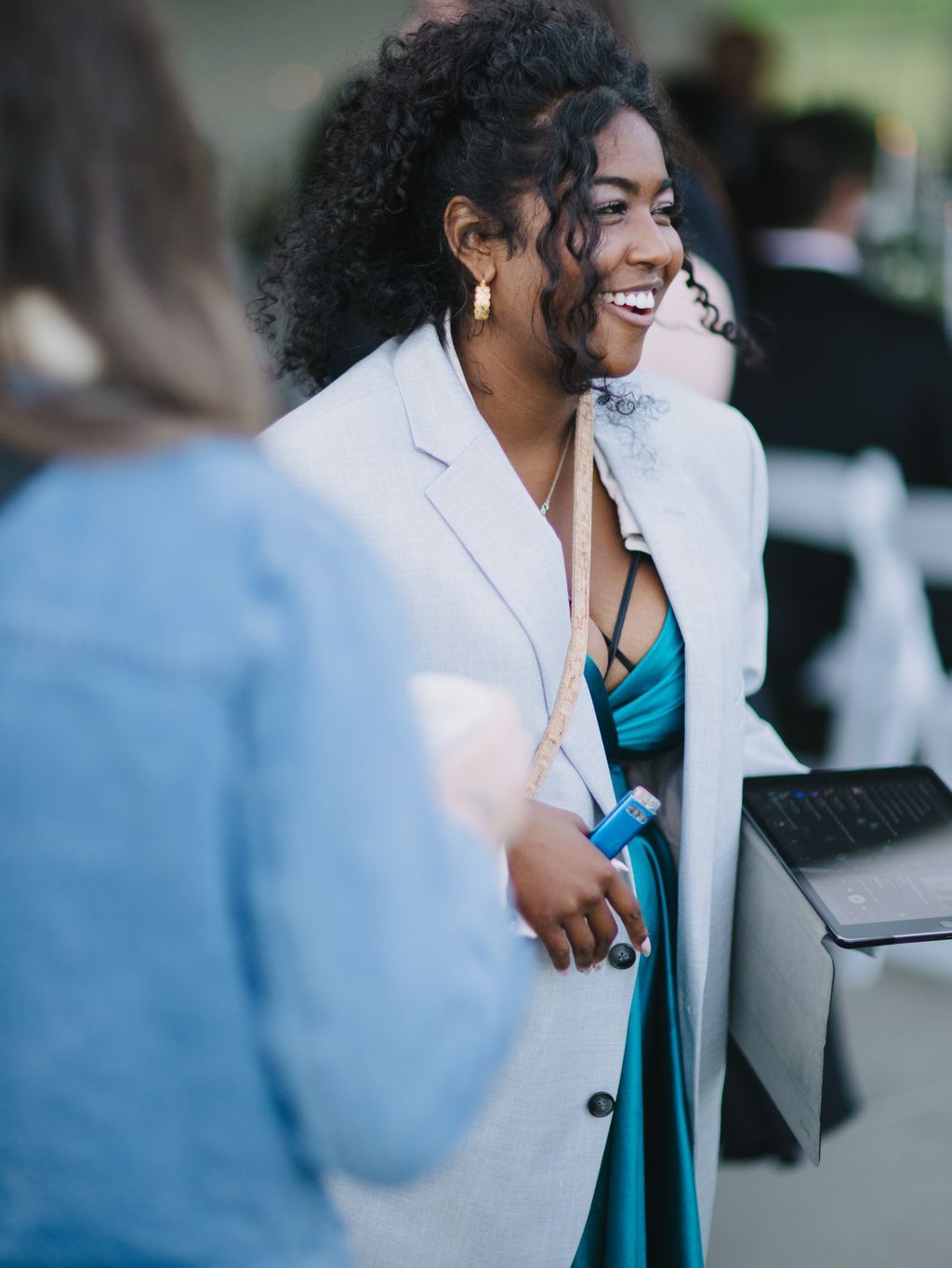 Bride in cream blazer and teal dress smiles while holding microphone at wedding ceremony