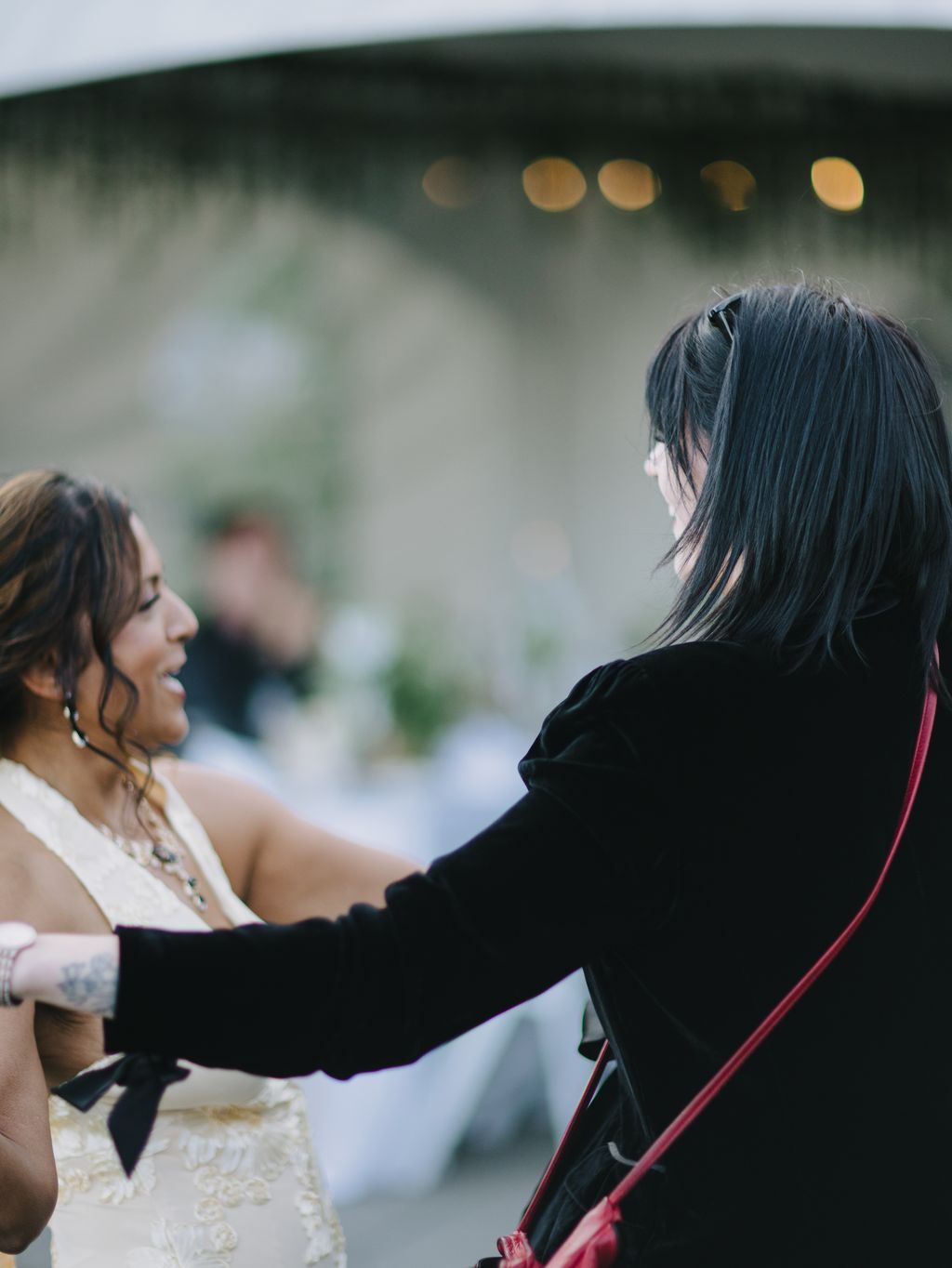 Bride in black jacket seen from behind, soft bokeh lights in misty background, intimate wedding moment