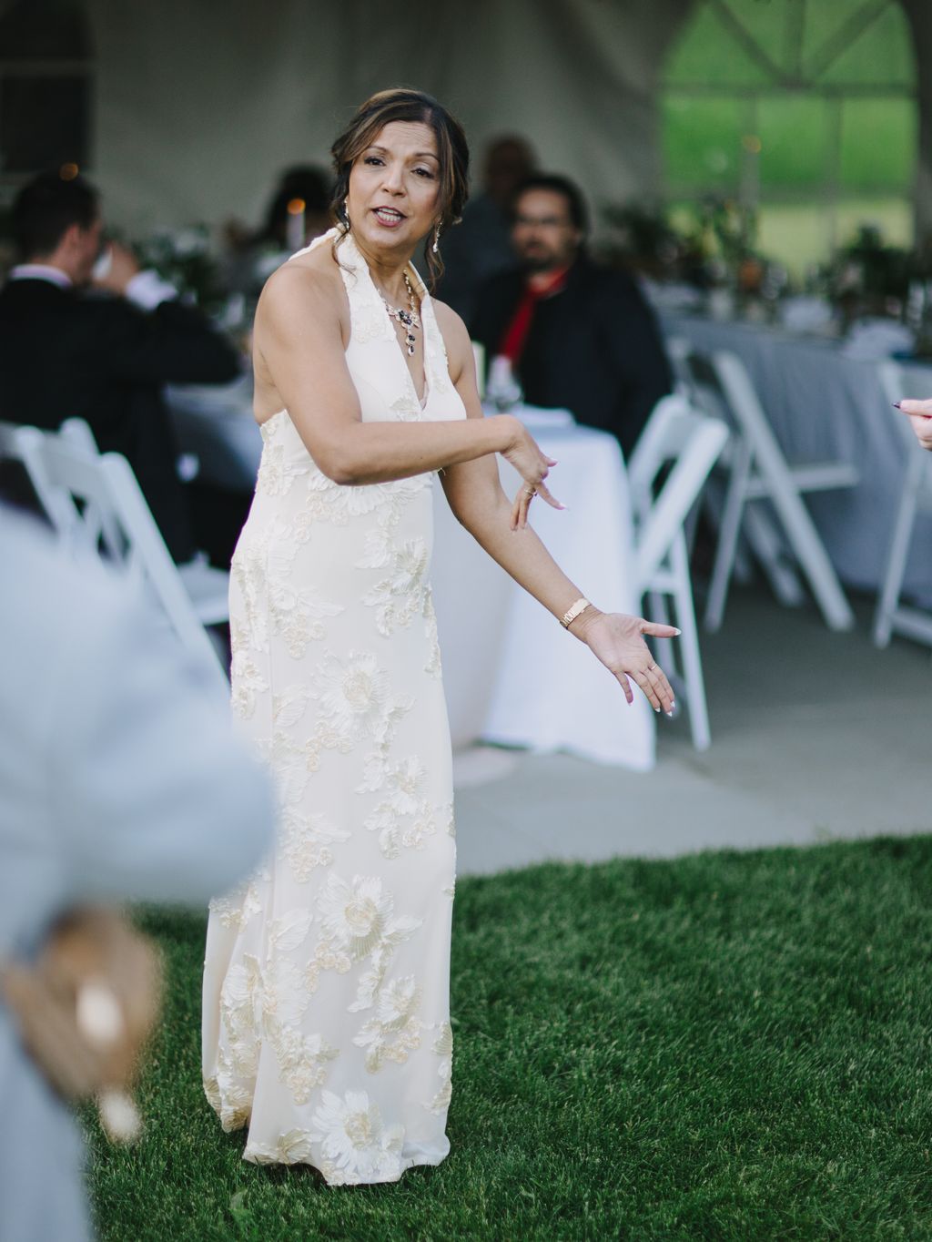 Bride in ivory beaded halter gown smiles at camera on manicured lawn during outdoor wedding reception
