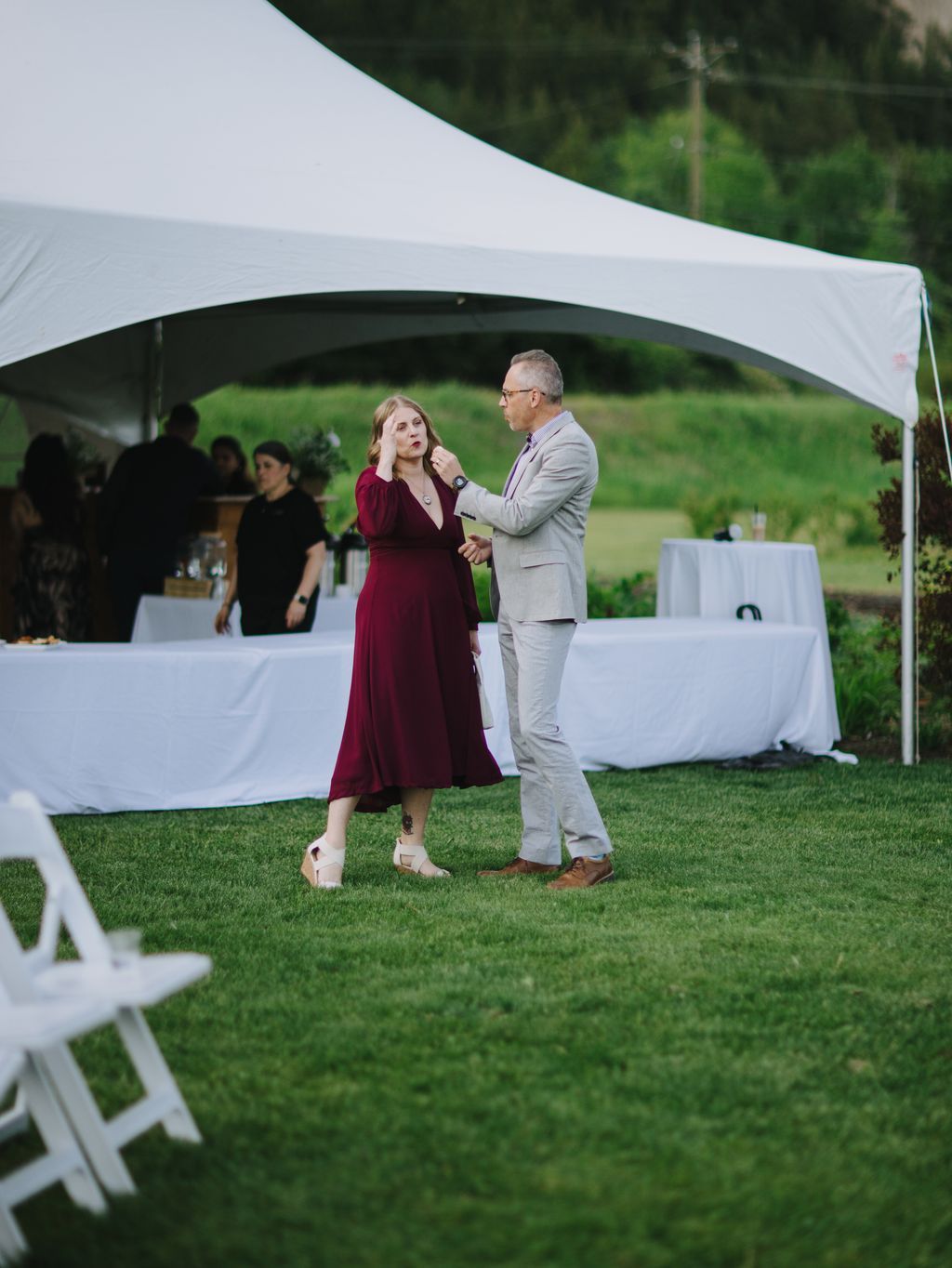 Couple dancing under white tent canopy at outdoor garden reception on green lawn