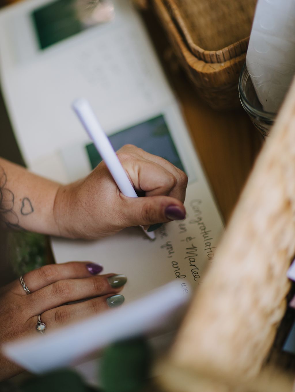 Close-up of hands holding a white pen over handwritten vows with manicured nails and brown fabric visible above