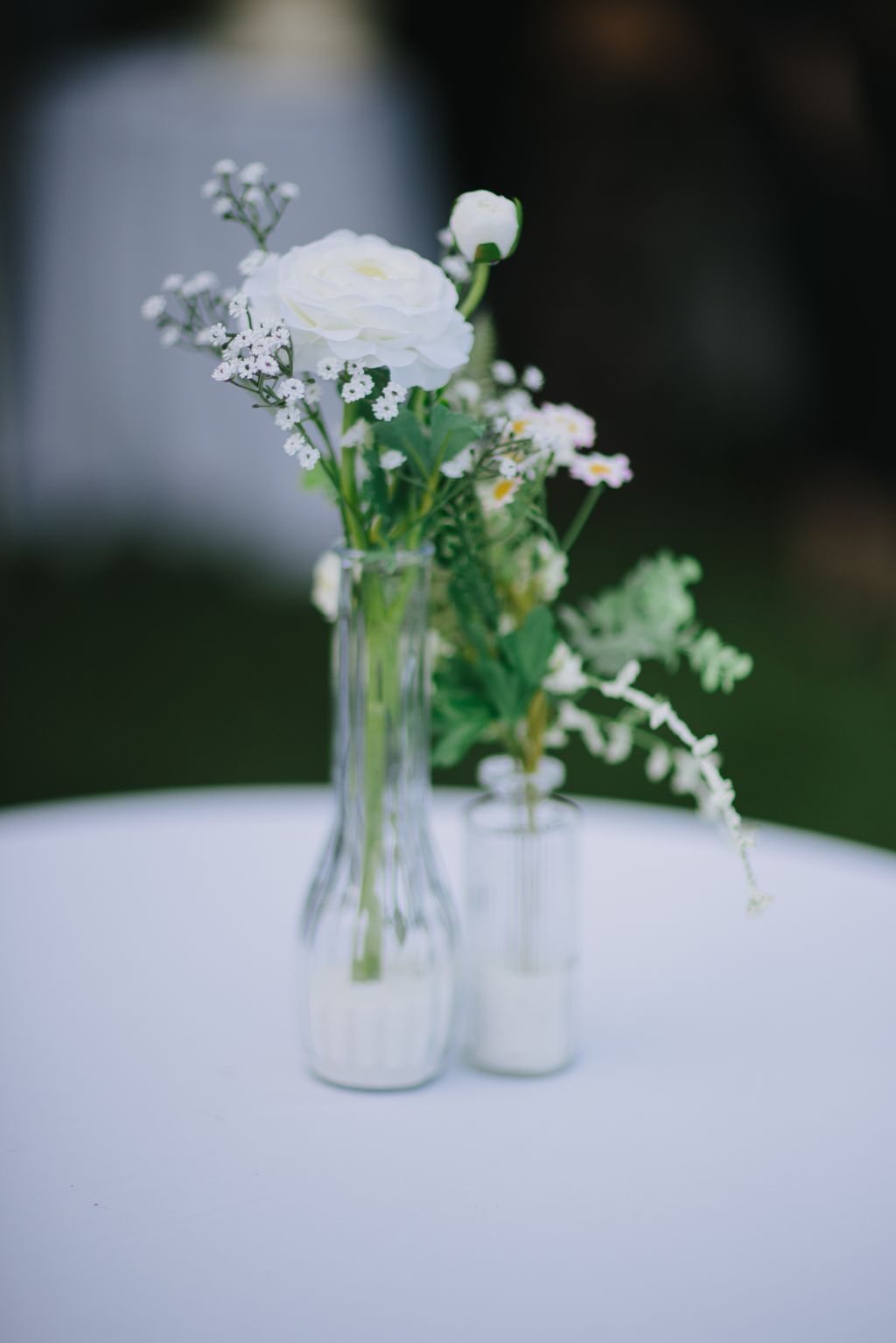 Delicate white ranunculus and baby''s breath in clear glass vases on white surface with soft-focused background