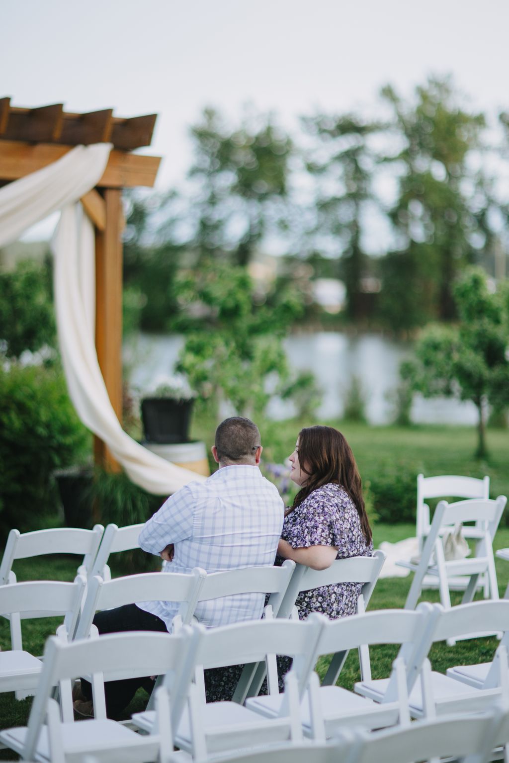 Couple sitting in white Adirondack chairs overlooking a blurred garden and water, soft natural light, intimate moment