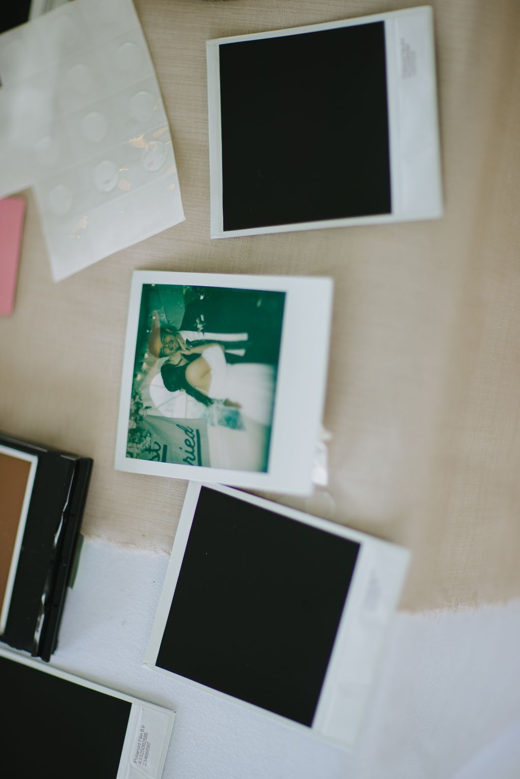 Scattered instant film prints on neutral linen, including a green-toned photo and blank black frames, arranged at varying angles