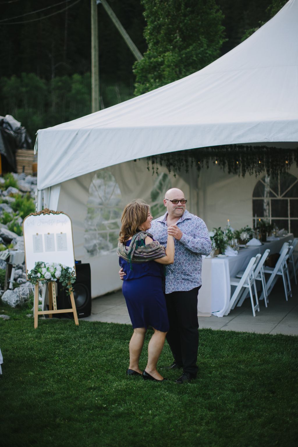 Couple dancing under white tent at outdoor garden reception with lush green backdrop