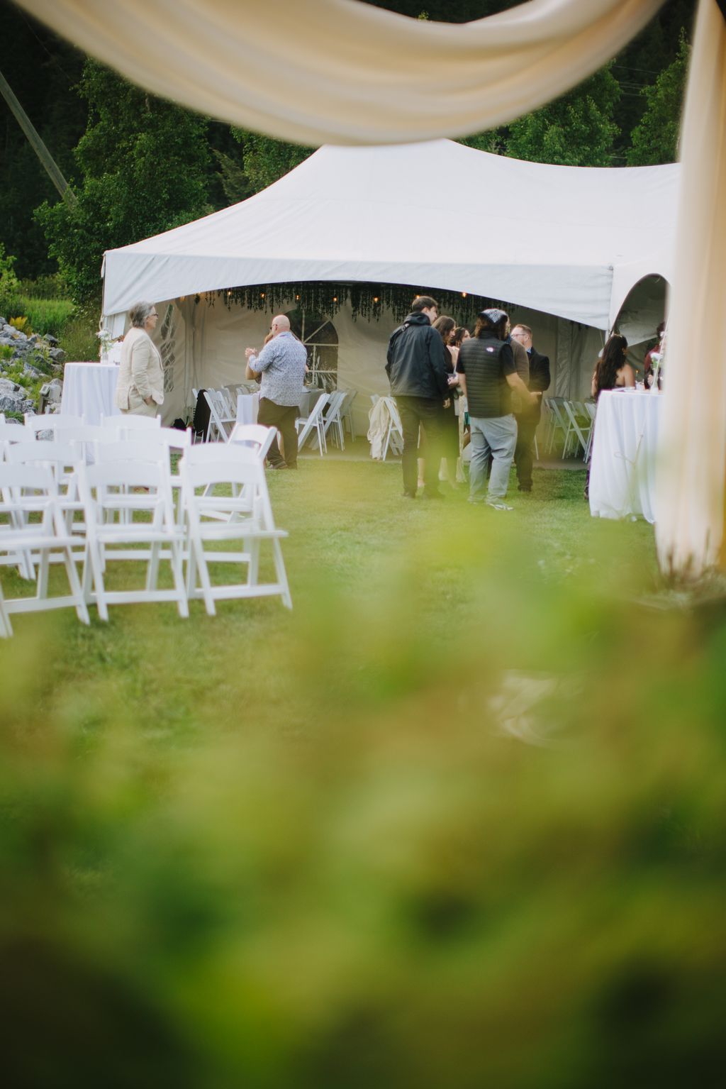 Guests mingling under a white marquee tent on a lush green lawn during an outdoor wedding reception
