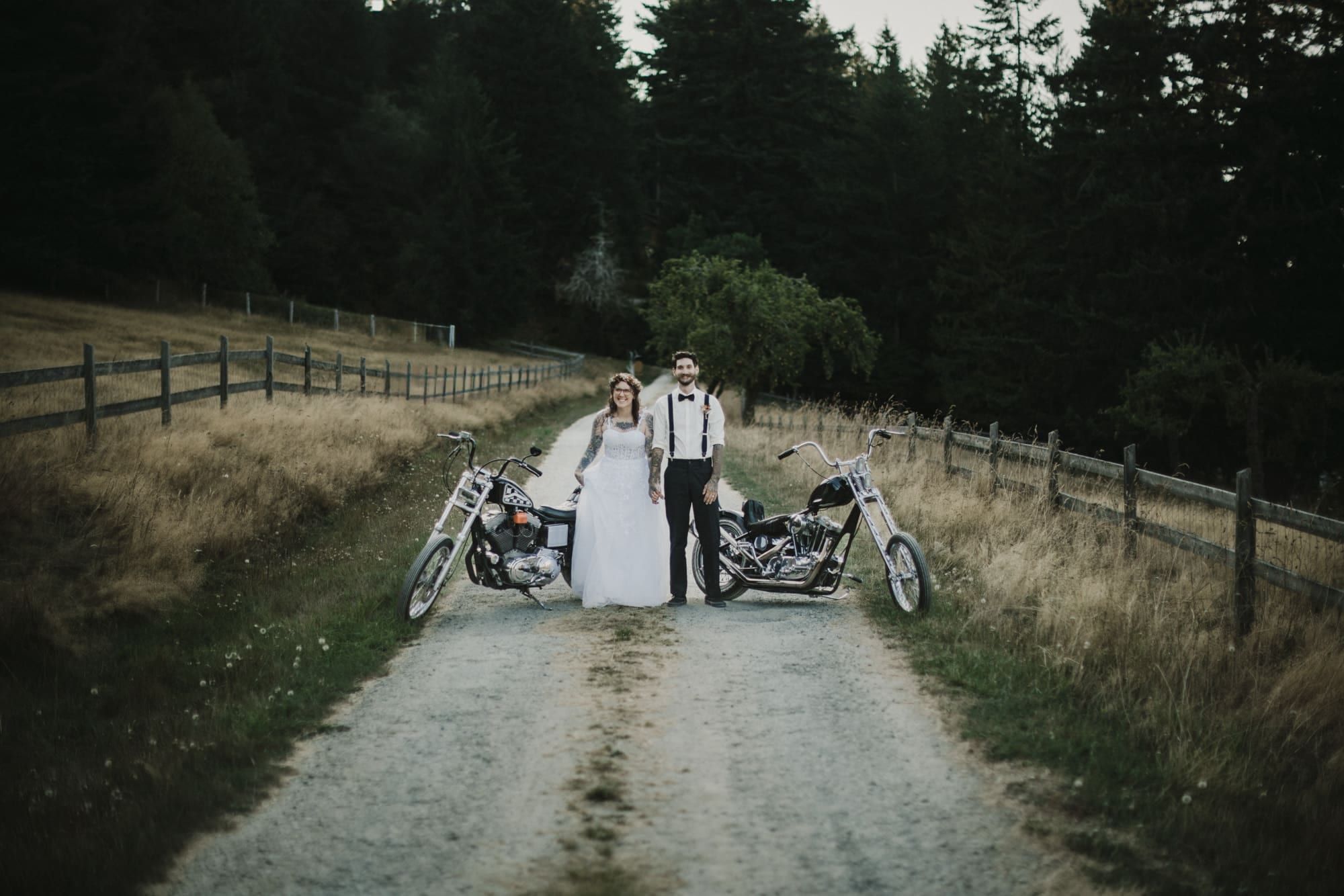 Newlyweds flanked by two motorcycles on a gravel road